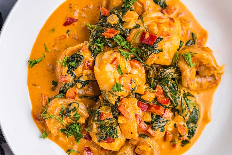 A plate of shrimp and spinach in a creamy red sauce.