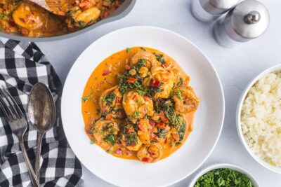 A dinner bowl with a helping of paprika shrimp next to cauliflower rice and salt and pepper mills.