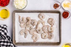 Raw shrimp on a tray seasoned with salt and pepper.