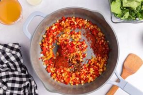 Spices in a skillet with cooked bell pepper and onion.