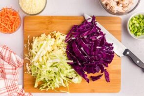 A wooden cutting board with chopped green and purple cabbage on it.