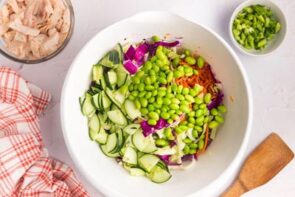 A white bowl with edamame, cucumber and purple cabbage.