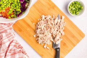 A cutting board with chopped cooked chicken next to a chef's knife.